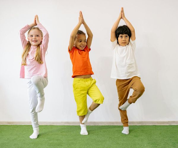 Child balancing on one leg in a tree yoga pose, smiling.